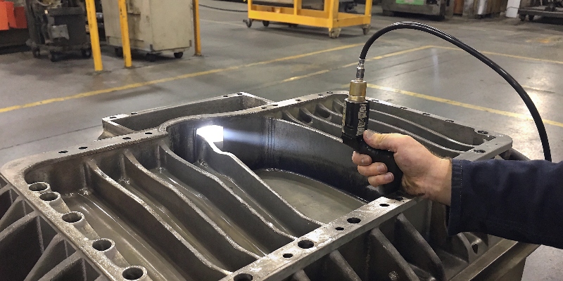 An operator using a handheld ultrasonic flaw detector probe on a thick-walled die-cast component.