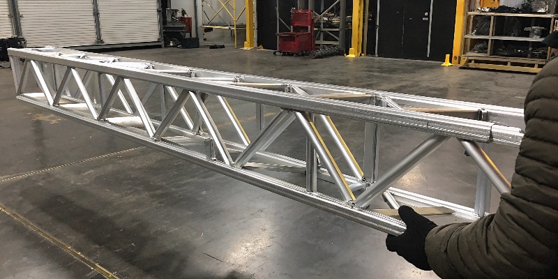 Una pieza estructural de aluminio ligera siendo sostenida con una mano para demostrar su bajo peso en comparación con su tamaño