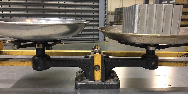 A scale balancing a lightweight aluminum part against a much smaller but equally heavy steel part