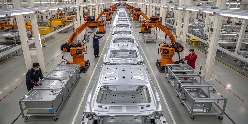 An assembly line of electric vehicle chassis, highlighting the numerous aluminum die cast components like battery trays and motor housings.