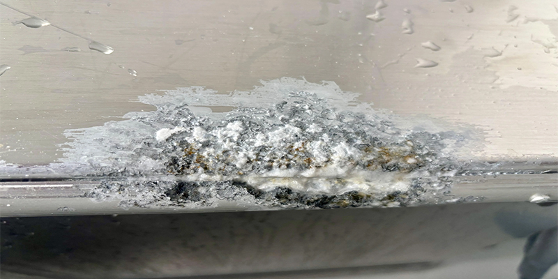 A close-up macro photograph showing the white, powdery texture of aluminum oxide corrosion on a metal part.