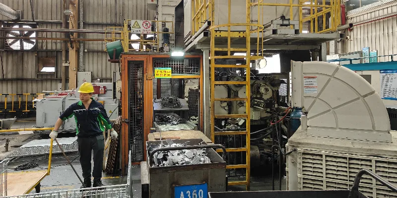 A robotic arm in a foundry extracting a newly formed, intricate aluminum motor housing cover from a die casting machine.