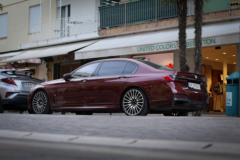 High-end maroon sedan parked outdoors at designer brand shop with urban setting.